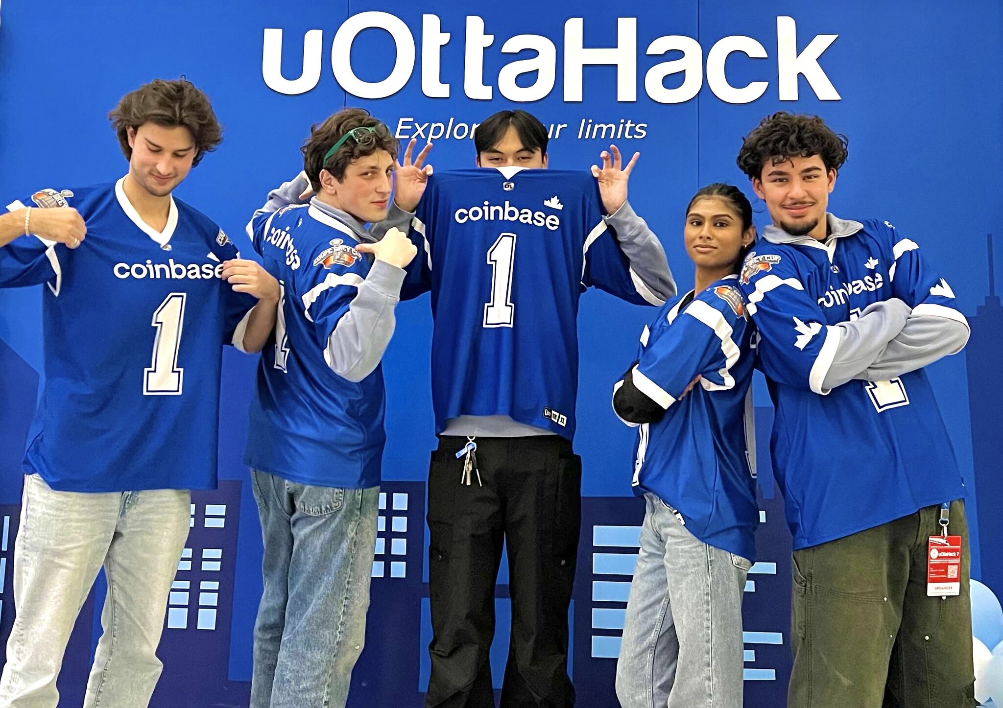 five uottahack organizers posing with coinbase-branded hockey jerseys in front of the uottahack backdrop